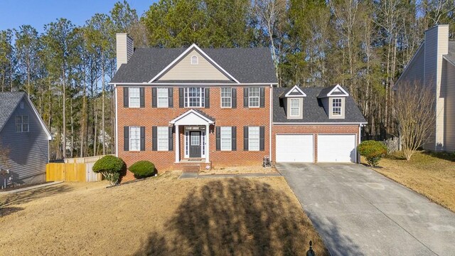 colonial house featuring brick siding, fence, a chimney, driveway, and an attached garage