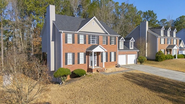 colonial house with a chimney, brick siding, an attached garage, and driveway