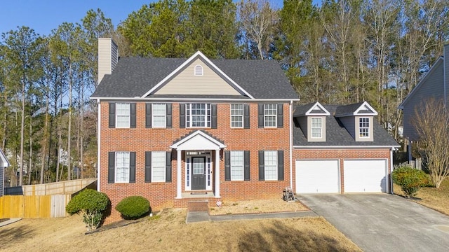 colonial home with brick siding, fence, a chimney, driveway, and an attached garage