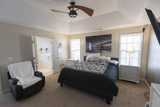 carpeted bedroom featuring visible vents, a ceiling fan, a tray ceiling, ensuite bath, and baseboards