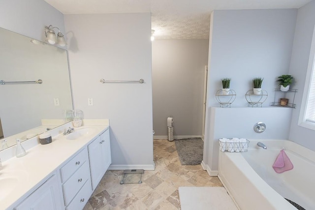 full bathroom featuring baseboards, double vanity, a sink, a textured ceiling, and a garden tub