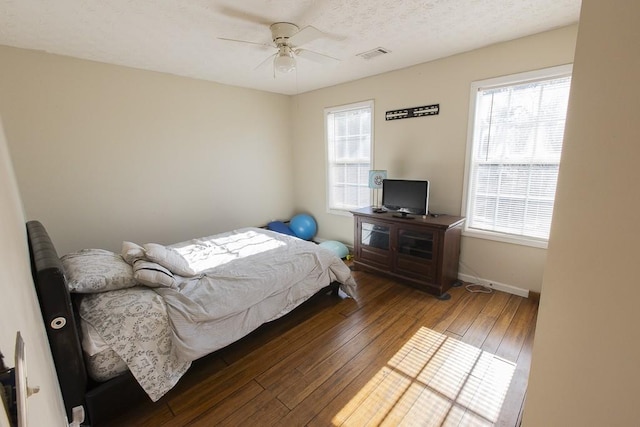 bedroom featuring a ceiling fan, baseboards, visible vents, hardwood / wood-style flooring, and a textured ceiling