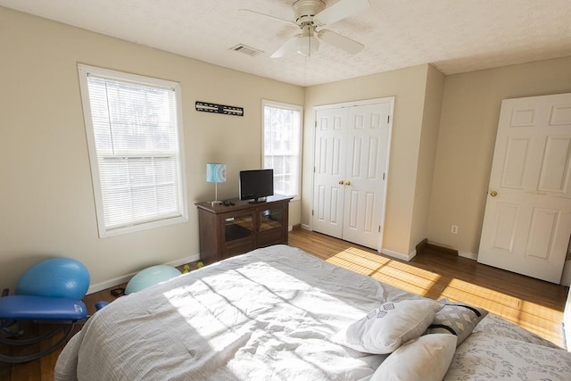 bedroom featuring a ceiling fan, visible vents, wood finished floors, baseboards, and a closet