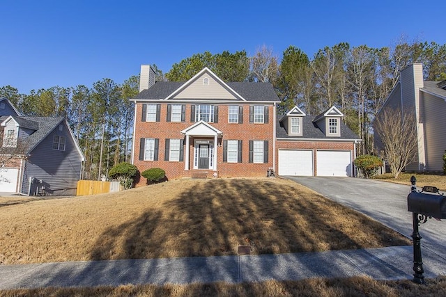 colonial home with brick siding, an attached garage, aphalt driveway, and fence