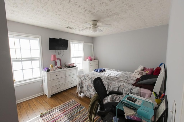 bedroom featuring hardwood / wood-style floors, baseboards, visible vents, ceiling fan, and a textured ceiling