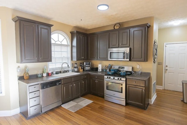 kitchen featuring light wood-type flooring, visible vents, a sink, dark countertops, and stainless steel appliances