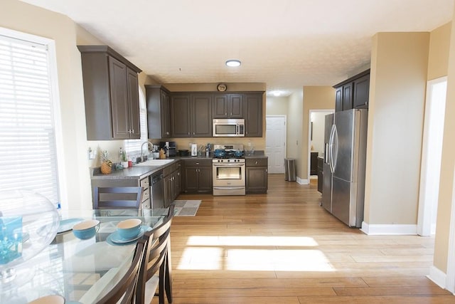 kitchen with baseboards, a sink, stainless steel appliances, dark brown cabinets, and light wood-type flooring