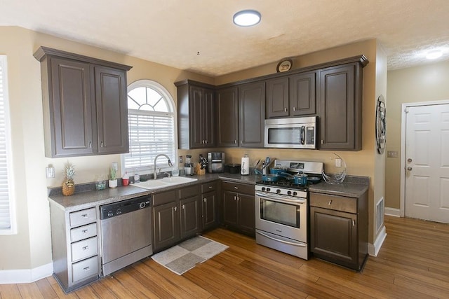 kitchen featuring a sink, dark brown cabinetry, appliances with stainless steel finishes, dark countertops, and light wood-type flooring