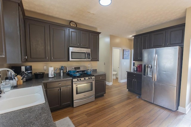 kitchen with a sink, dark countertops, light wood finished floors, and stainless steel appliances