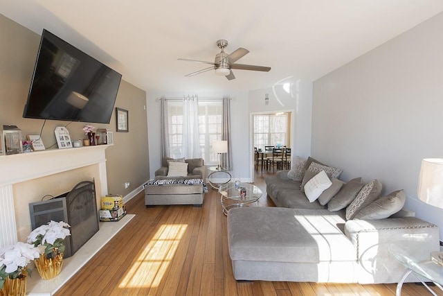 living room with a fireplace with raised hearth, baseboards, ceiling fan, and hardwood / wood-style floors