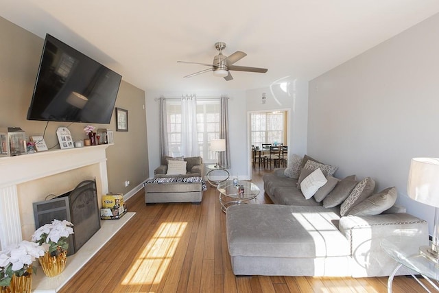 living area featuring a fireplace with raised hearth, a ceiling fan, baseboards, and hardwood / wood-style floors