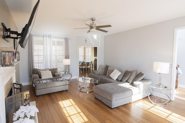 living area with a fireplace, a ceiling fan, baseboards, and wood-type flooring