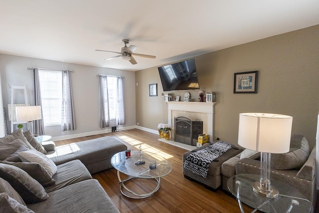 living area with a tiled fireplace, wood finished floors, baseboards, and a ceiling fan