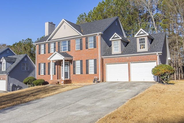 colonial home featuring driveway, roof with shingles, a garage, brick siding, and a chimney