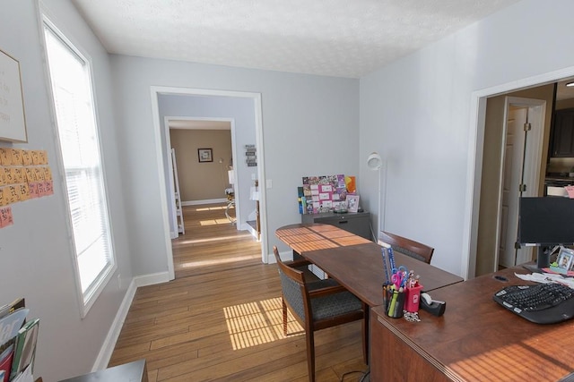 home office with a wealth of natural light, baseboards, a textured ceiling, and light wood-style floors