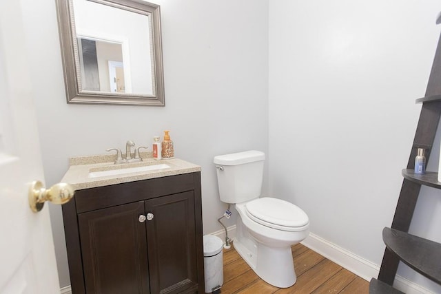 half bathroom featuring baseboards, toilet, wood finished floors, and vanity