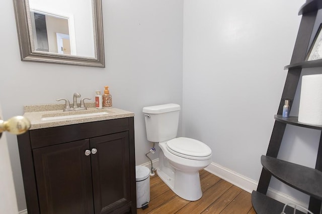 bathroom with toilet, vanity, baseboards, and wood finished floors