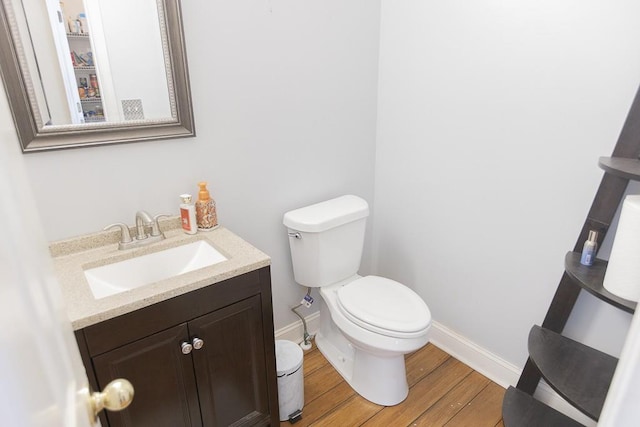 bathroom featuring toilet, vanity, baseboards, and wood finished floors