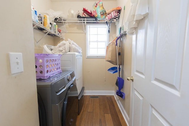 clothes washing area featuring dark wood finished floors, laundry area, washing machine and dryer, and baseboards