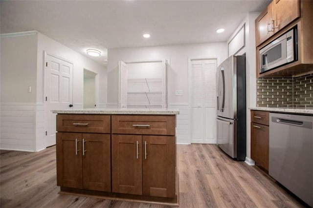 280 Hitchcock Rd, Dallas, GA 30157 - kitchen featuring appliances with stainless steel finishes, a wainscoted wall, light wood-style floors, light stone countertops, and a center island
