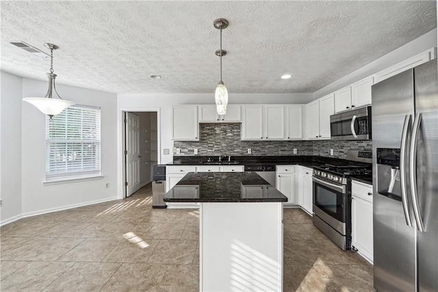 kitchen with a kitchen island, tasteful backsplash, white cabinetry, appliances with stainless steel finishes, and decorative light fixtures