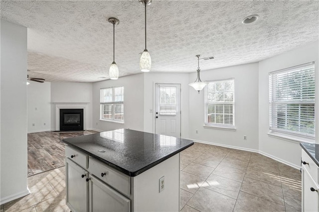 kitchen with ceiling fan, light tile patterned floors, a kitchen island, a textured ceiling, and decorative light fixtures