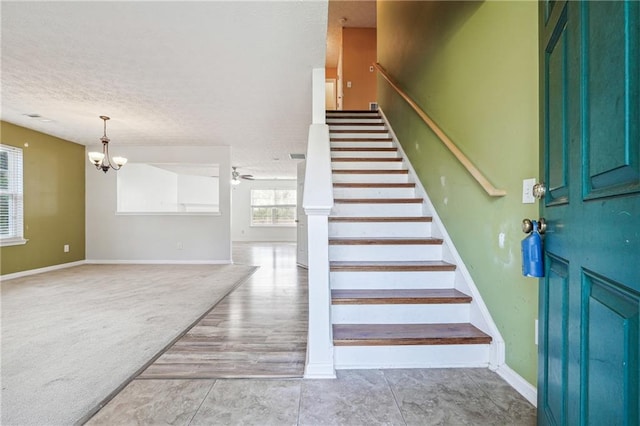 stairs featuring ceiling fan with notable chandelier, carpet, and a textured ceiling