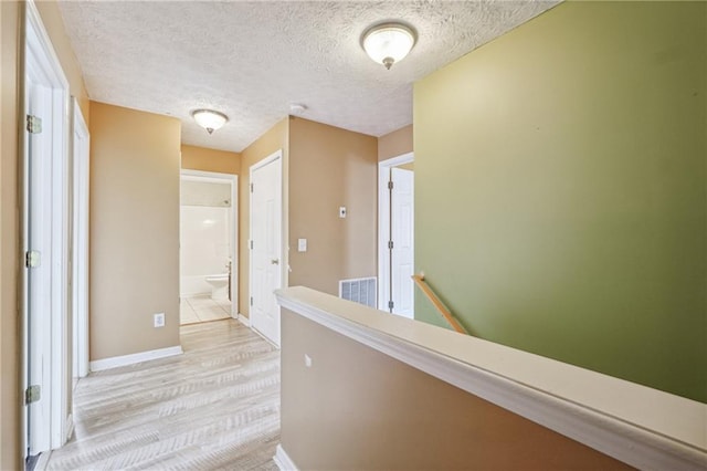 corridor featuring light wood-type flooring and a textured ceiling