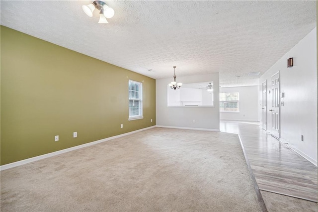 spare room with light carpet, a textured ceiling, and a notable chandelier