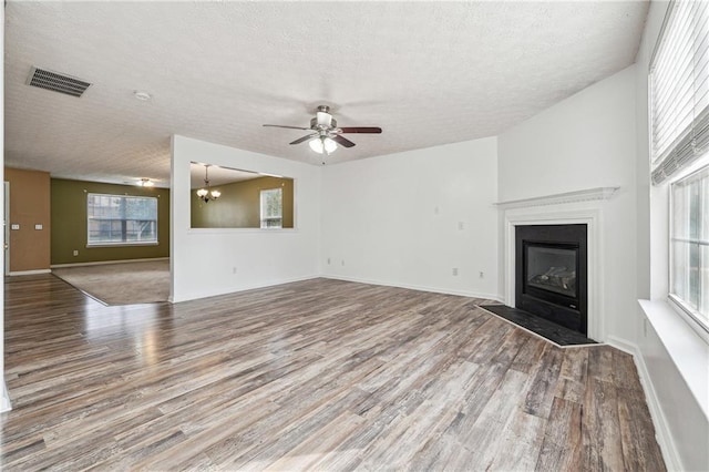 unfurnished living room with ceiling fan with notable chandelier, hardwood / wood-style floors, a wealth of natural light, and a textured ceiling