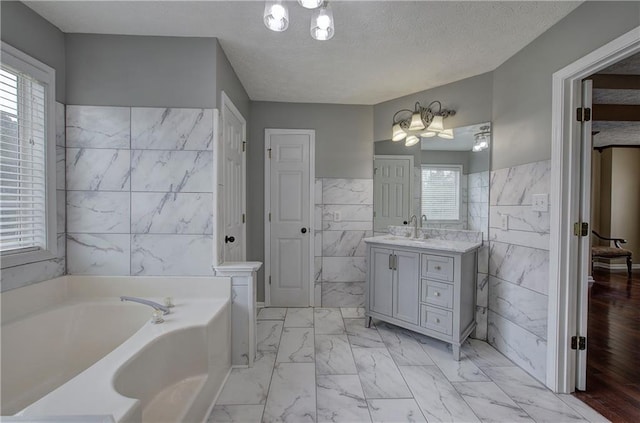 bathroom with tile walls, vanity, a bath, and a textured ceiling