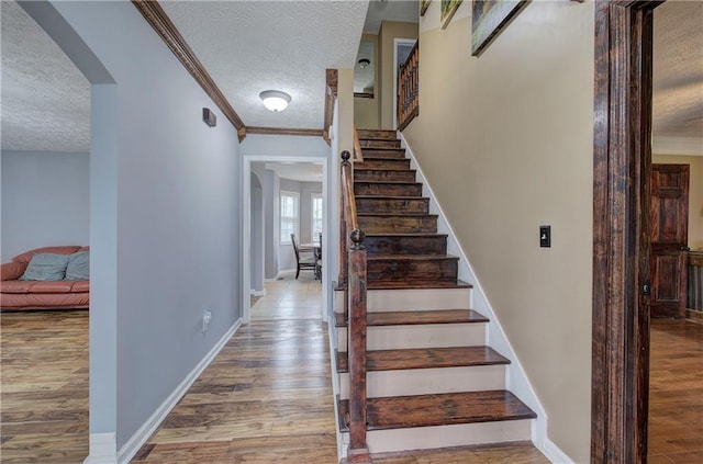 stairway featuring wood-type flooring, ornamental molding, and a textured ceiling