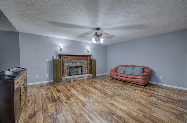 unfurnished living room with ceiling fan, wood-type flooring, a stone fireplace, and a textured ceiling