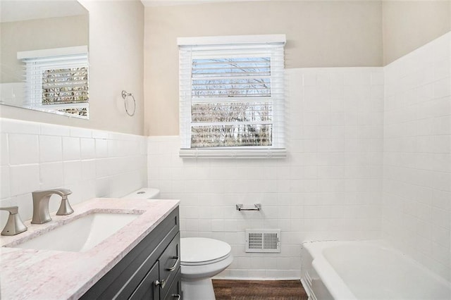 bathroom with vanity, toilet, tile walls, wood-type flooring, and a tub