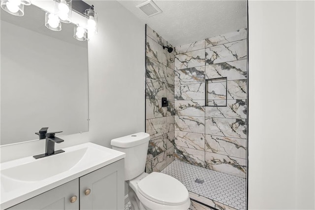 bathroom with vanity, a tile shower, a textured ceiling, and toilet