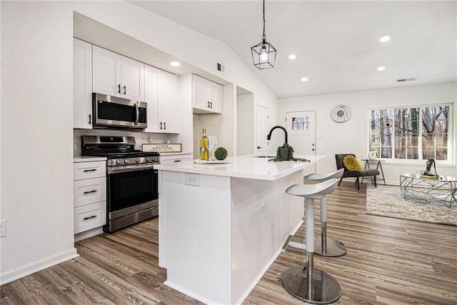 kitchen with decorative light fixtures, white cabinetry, lofted ceiling, stainless steel appliances, and a center island with sink