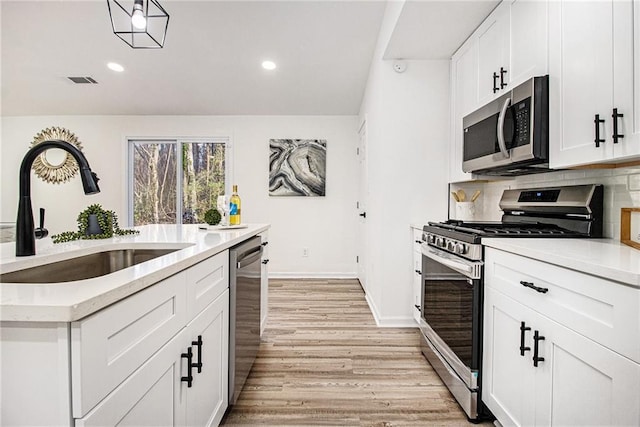 kitchen with sink, white cabinetry, tasteful backsplash, light wood-type flooring, and appliances with stainless steel finishes