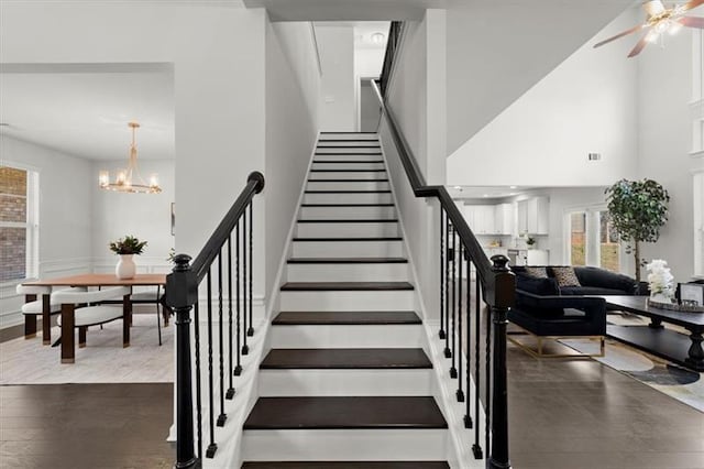 staircase with a high ceiling, ceiling fan with notable chandelier, and wood finished floors