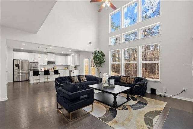 living room with dark wood-type flooring, baseboards, ceiling fan, and a high ceiling