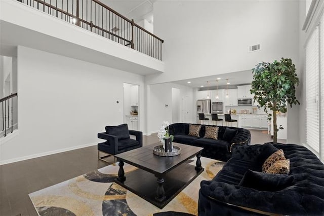 living area featuring baseboards, a high ceiling, light wood-style flooring, and visible vents