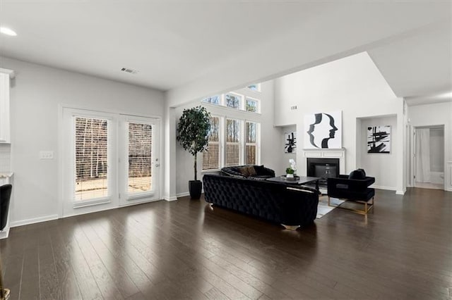 living area featuring baseboards, a glass covered fireplace, dark wood-style floors, and visible vents
