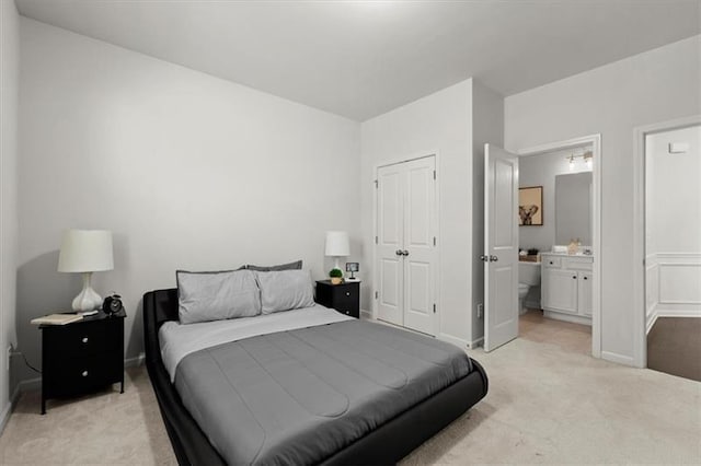 bedroom featuring a closet, baseboards, ensuite bath, and light carpet