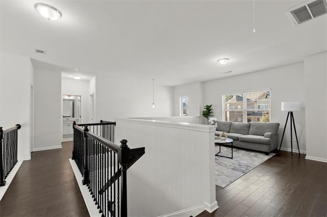 hall with baseboards, visible vents, dark wood-style floors, and an upstairs landing