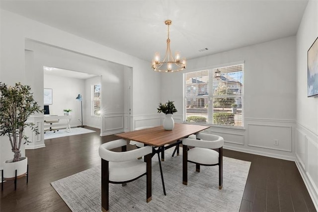 dining area with a healthy amount of sunlight, a wainscoted wall, dark wood-style floors, and a chandelier