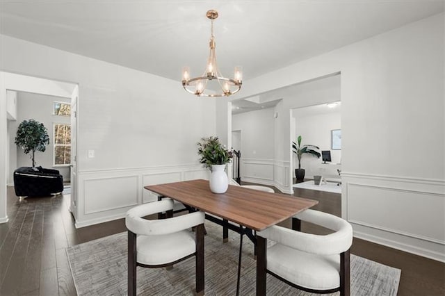 dining space featuring wainscoting, a decorative wall, a notable chandelier, and dark wood-style floors
