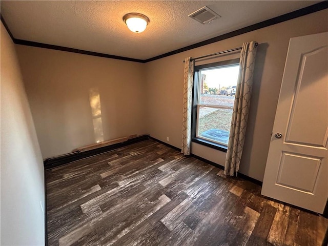 spare room featuring visible vents, dark wood-type flooring, ornamental molding, a textured ceiling, and baseboards