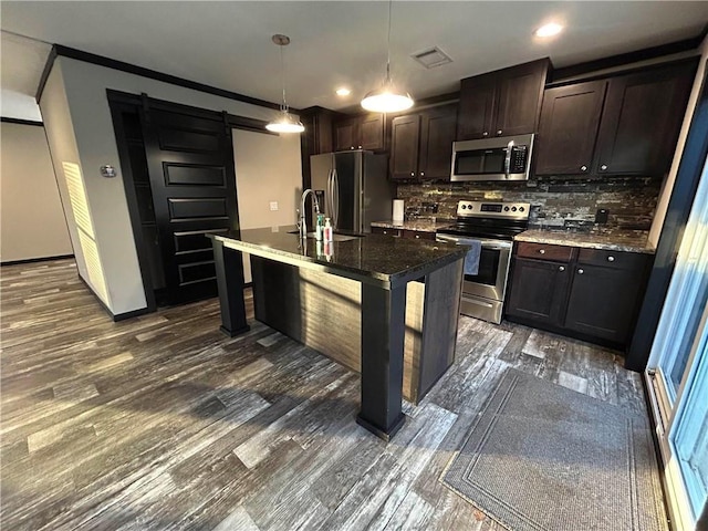 kitchen with dark wood finished floors, stainless steel appliances, a barn door, dark brown cabinetry, and decorative backsplash