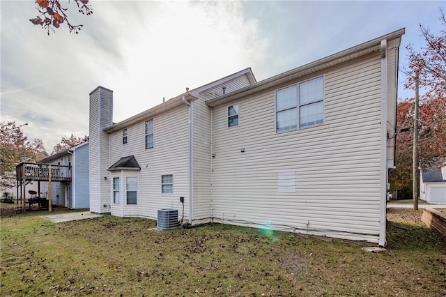 rear view of property featuring a lawn, central air condition unit, a wooden deck, and a patio