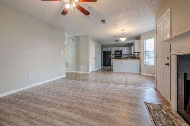 unfurnished living room with a textured ceiling, light hardwood / wood-style floors, and ceiling fan