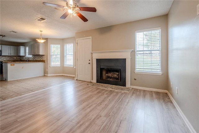 unfurnished living room featuring a textured ceiling, light hardwood / wood-style floors, ceiling fan, and sink